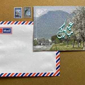 May include: An Air Mail envelope with red, white, and blue stripes and the words "Air Mail" in a red box. A postcard with a mountain scene and Arabic script is next to the envelope, along with two postage stamps.