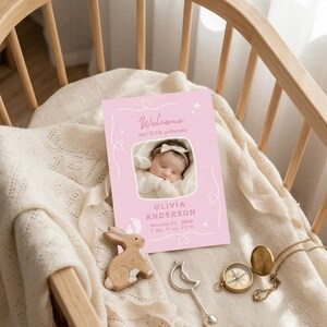Puede incluir: Una tarjeta rosa de anuncio de beb&eacute; con el texto "Welcome our little princess" y una foto de un beb&eacute; durmiendo. La tarjeta tambi&eacute;n incluye el nombre del beb&eacute;, la fecha de nacimiento y el peso: 3,49 kg, 50,8 cm. Un conejito de madera, un sonajero plateado y una br&uacute;jula tambi&eacute;n son visibles.