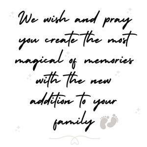 May include: A white sign featuring black cursive text that reads: We wish and pray you create the most magical of memories with the new addition to your family. The design includes small grey star icons and a pair of grey baby footprints at the bottom.