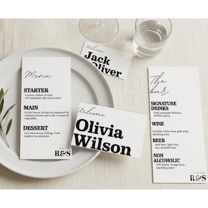 Puede incluir: Una mesa de boda minimalista con tarjetas de men&uacute; blancas, tarjetas de lugar y un men&uacute; de bar. El men&uacute; enumera opciones de entrantes, platos principales y postres. Las tarjetas de lugar dicen "Jack Oliver" y "Olivia Wilson". El men&uacute; del bar enumera bebidas.
