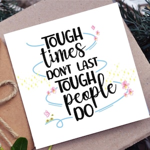 May include: A white greeting card with the text "TOUGH times DON'T LAST TOUGH people DO" in black script. The card is decorated with light blue swirls, pink flowers, and yellow starbursts. The card is on a brown surface.