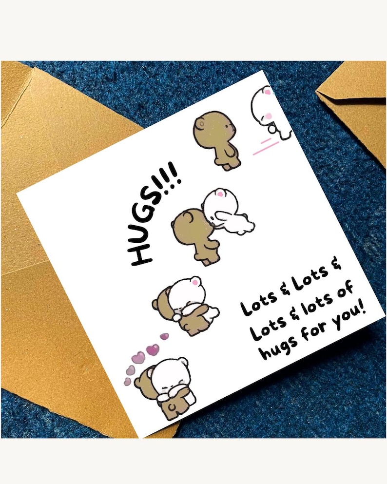 May include: A white greeting card with the words "HUGS!!!" and "Lots & Lots & Lots & lots of hugs for you!" in black text. The card features cartoon bears hugging, with pink hearts. The card is placed on a blue surface.