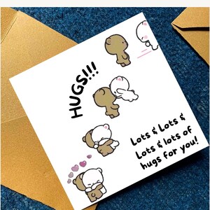 Puede incluir: Una tarjeta de felicitaci&oacute;n cuadrada de color blanco con ilustraciones de dibujos animados de un oso pardo y un oso blanco abraz&aacute;ndose. El texto dice HUGS!!! y Lots & Lots & Lots & lots of hugs for you! La tarjeta est&aacute; entre dos sobres color canela.
