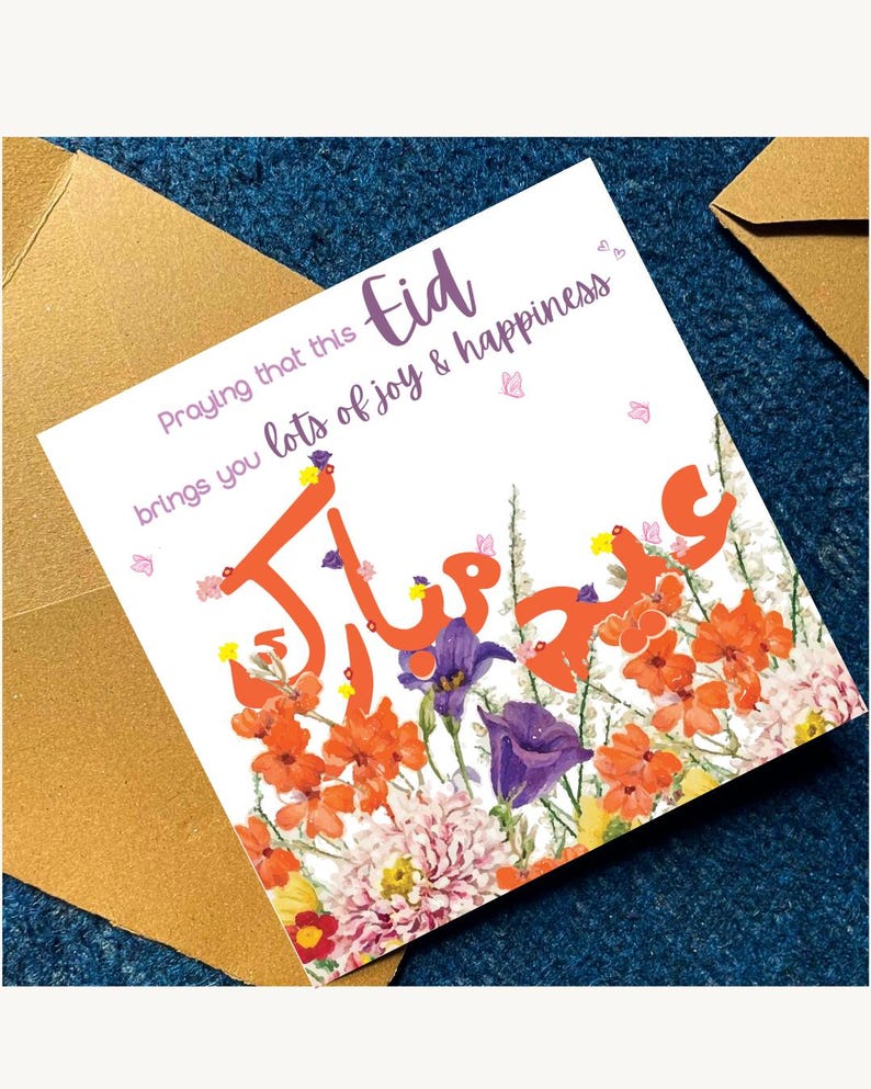 Op de afbeelding: Een witte wenskaart met het woord "Eid" in paarse letters en oranje Arabische kalligrafie. De kaart is versierd met oranje, paarse en roze bloemen. De tekst "Praying that this brings you lots of joy & happiness" staat ook op de kaart.