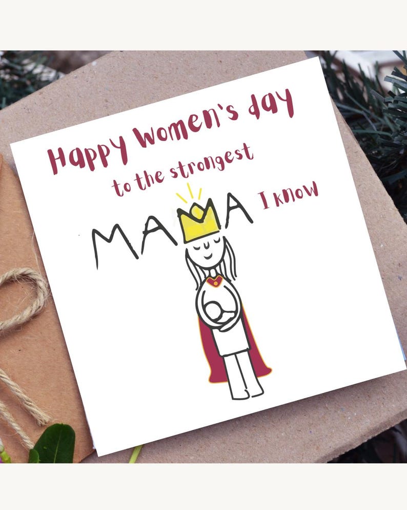 May include: A greeting card with the text "Happy Women's Day to the strongest MAMA I know." The card features a simple illustration of a woman wearing a crown and cape, holding a baby. The card is on a brown surface.