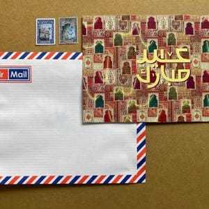 May include: An Air Mail envelope with red, white, and blue striped borders, a matching postcard with gold Arabic text, and three postage stamps. The postcard features a colourful geometric pattern.