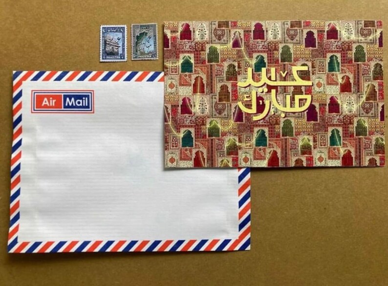 May include: An Air Mail envelope with red, white, and blue striped borders, a matching postcard with gold Arabic text, and three postage stamps. The postcard features a colourful geometric pattern.