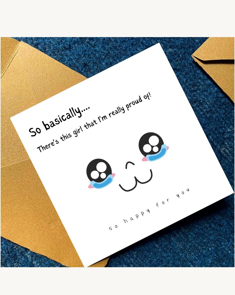 May include: A white greeting card with a cartoon face and the text "So basically.... There's this girl that I'm really proud of! So happy for you." The card is on a blue surface with a gold envelope.