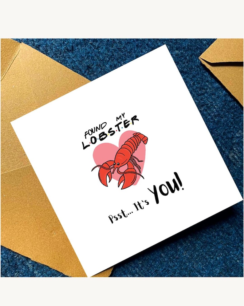Pu&ograve; includere: Un biglietto d'auguri quadrato bianco con un'illustrazione di un'aragosta rossa centrata sopra un cuore rosa. Il testo recita "FOUND MY LOBSTER" in lettere nere con punti colorati e "Psst... It's YOU!" in corsivo nero. Accompagnato da buste marroni.