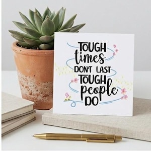 May include: A white card with the text "TOUGH times DON'T LAST TOUGH people DO" in black script, decorated with blue swirls and pink flowers. A succulent plant in a terracotta pot and a gold pen are also visible.