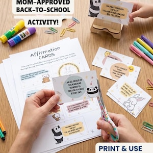 May include: A set of printable affirmation cards featuring cartoon characters and encouraging text. The cards are displayed on paper sheets, with some being cut out using patterned scissors. Includes glue sticks, colourful paper clips, and a wooden stand.