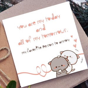May include: A white greeting card with the text "you are my today and all of my tomorrows, my favorite person to annoy" in pink and brown. Two cartoon cat characters are embracing at the bottom right.