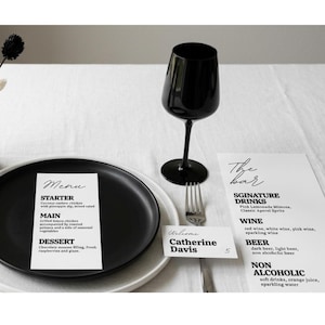 Puede incluir: Una copa de vino negra, un tenedor y un plato sobre un mantel blanco. Tambi&eacute;n hay una tarjeta de men&uacute; y una carta de bebidas. La tarjeta del men&uacute; enumera un entrante, un plato principal y un postre. La carta de bebidas enumera bebidas de autor, vino, cerveza y bebidas sin alcohol.