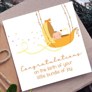 May include: A greeting card with a baby-themed illustration. The card features a cartoon baby in a yellow cradle, with the words "Congratulations on the birth of your little bundle of joy" written in orange script.