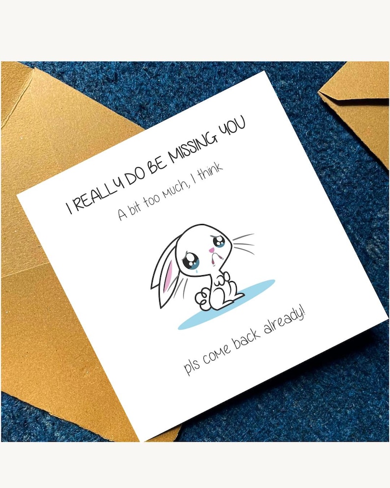 May include: A square white greeting card featuring a cartoon illustration of a sad, crying white rabbit with pink inner ears. The text reads: I REALLY DO BE MISSING YOU, A bit too much, I think, and pls come back already! The card is paired with a brown envelope.