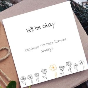 Puede incluir: Una tarjeta de felicitaci&oacute;n cuadrada de color blanco con el texto en negro it'll be okay because i'm here foryou always. El borde inferior muestra una fila de flores dibujadas con l&iacute;neas negras, con una sola flor resaltada en amarillo.