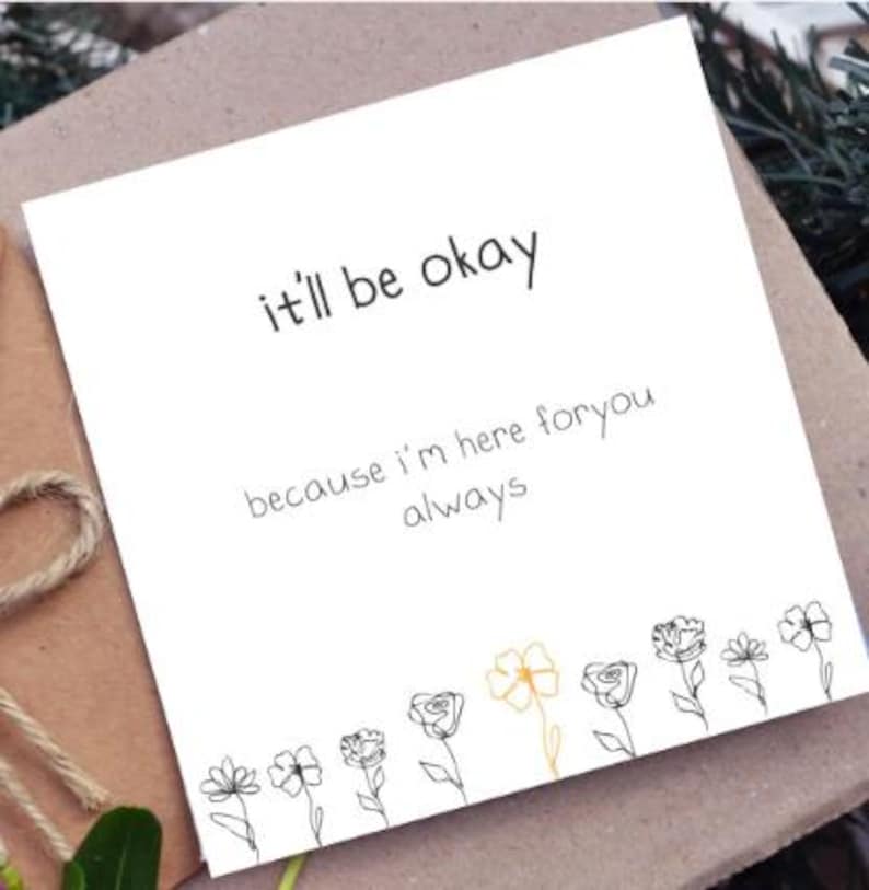 Puede incluir: Una tarjeta de felicitaci&oacute;n cuadrada de color blanco con el texto en negro it'll be okay because i'm here foryou always. El borde inferior muestra una fila de flores dibujadas con l&iacute;neas negras, con una sola flor resaltada en amarillo.