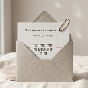 Puede incluir: Una tarjeta de felicitaci&oacute;n en un sobre marr&oacute;n claro. La tarjeta dice: "Just wanted to remind you that you mean THIIIIIIIIIIIIIIIS MUUUUCHHHHHH TO ME." Un clip dorado sujeta la tarjeta. El sobre est&aacute; abierto.