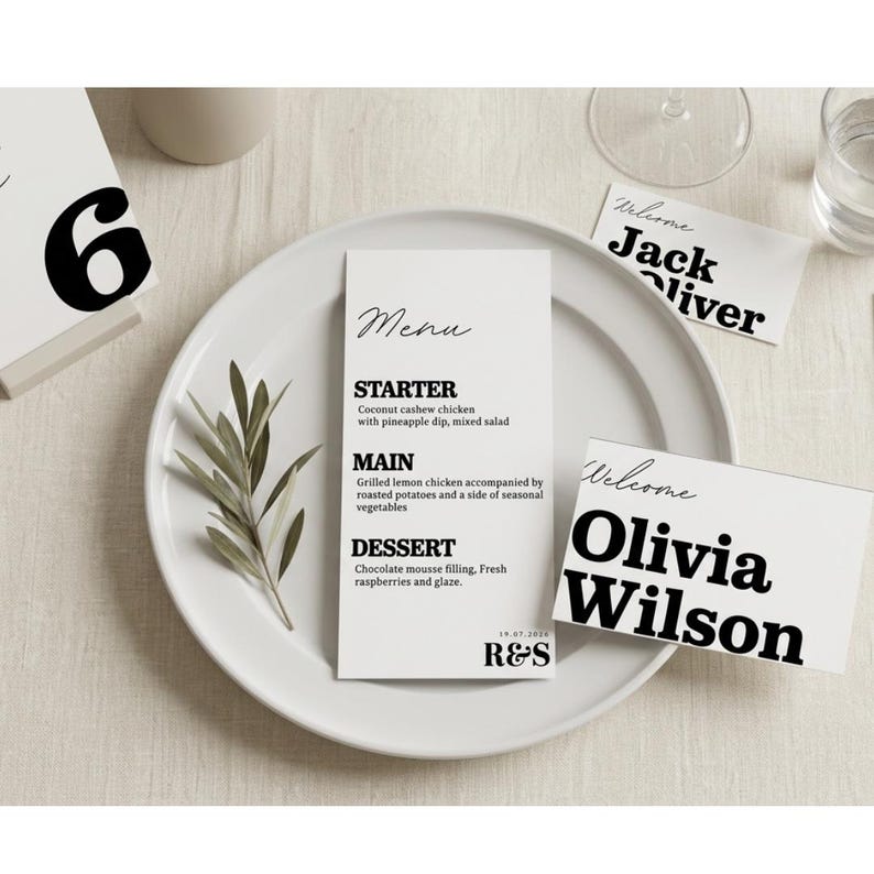 Op de afbeelding: Een witte plaat met een menukaart, een tafelnummer en twee naamkaarten. De menukaart bevat een voorgerecht, hoofdgerecht en dessert. De naamkaarten zeggen "Welkom" en de namen "Jack Oliver" en "Olivia Wilson".