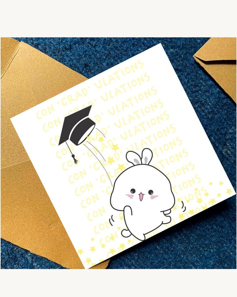 May include: A graduation card with a cartoon bunny and mortarboard illustration. The card has the words "CON GRAD ULATIONS" in a repeating pattern. The card is white with yellow accents and is placed on a blue surface.