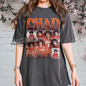 May include: Dark gray t-shirt featuring the name "CHAD" in orange and red lettering. The shirt includes images of a person in a red basketball jersey with the name "DANFORTH" below the images. The shirt has a vintage, distressed look.