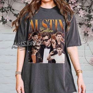 May include: Dark gray t-shirt featuring a vintage-style graphic of Austin Butler. The design includes the name "Austin Butler" in gold lettering, along with multiple images of the actor. The shirt has a classic crew neck and short sleeves.
