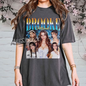 Puede incluir: Camiseta gris oscuro con un gráfico de Brooke Monk y el texto "Brooke Monk" en un diseño degradado. El gráfico incluye múltiples imágenes de Brooke Monk. La camiseta es de cuello redondo.