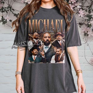 May include: Dark grey t-shirt with a collage of Michael B. Jordan images and gold text reading "MICHAEL B. JORDAN". The shirt has a vintage, worn appearance.