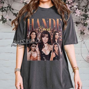 Puede incluir: Camiseta gris oscuro con un gráfico de Hande Erçel y su nombre en dorado. El diseño incluye varias imágenes de la actriz. La camiseta tiene un aspecto vintage y desgastado.