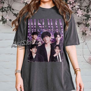 May include: Dark gray t-shirt featuring a graphic of the South Korean singer Im Si-wan. The design includes the name "IM SI-WAN" in a purple, retro font, and several images of the singer. The shirt has a vintage, worn look.