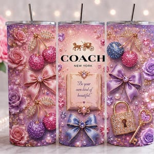 May include: A cylindrical tumbler with a straw featuring a pink and purple gradient background, decorated with glittery cherries, roses, bows, a gold padlock, a key, and the Coach New York logo with the text Be your own kind of beautiful.