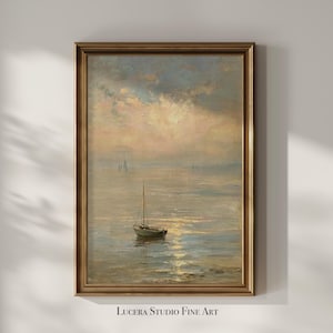 May include: A framed vertical wall art print featuring a sailboat on calm water under a soft, hazy sunset sky with muted gold, blue, and grey tones. The text Lucera Studio Fine Art is printed in black at the bottom center of the frame.