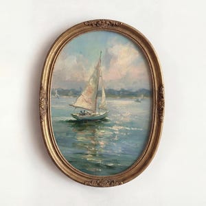 May include: An oval-shaped painting in a decorative gold frame depicting a sailboat on blue water under a cloudy sky. The artwork features visible brushstrokes and a maritime scene with a distant shoreline, captured in a classic, ornate frame.