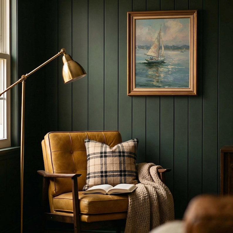 May include: A tan leather armchair with a plaid throw pillow and an open book, positioned next to a brass floor lamp. A framed painting of a sailboat on water hangs on a dark green paneled wall, creating a cozy seating area with warm lighting.