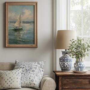 May include: A framed oil painting of a sailboat on water, a beige sofa with two patterned throw pillows, a wooden side table, a blue and white ceramic lamp with a beige shade, and a blue and white ceramic planter with a green plant.