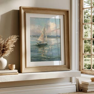 May include: A framed painting of a sailboat on calm water under a soft, cloudy sky. The artwork features muted blue and white tones, depicting a single vessel with sails raised. It is encased in a light-toned wooden frame with a white mat border.