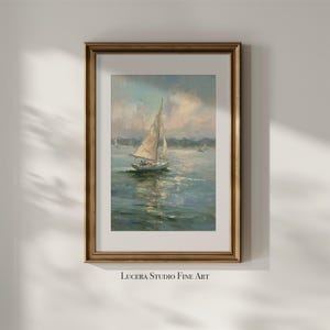May include: A framed art print featuring an oil painting of a sailboat on calm water under a soft, cloudy sky. The artwork is enclosed in a metallic gold frame with a white mat border. The text Lucera Studio Fine Art is printed below the frame.