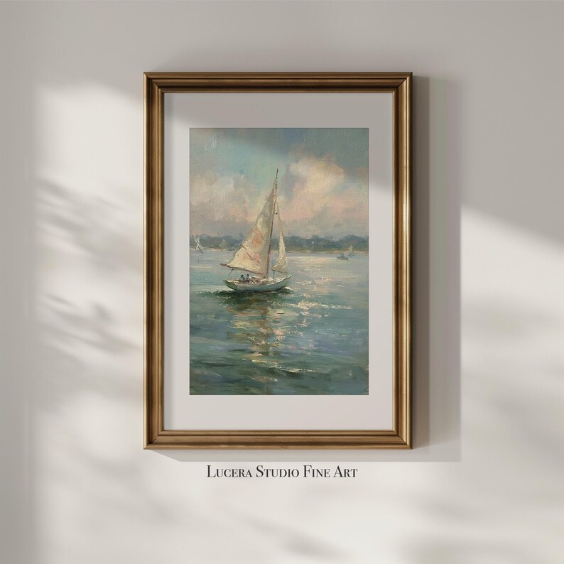 May include: A framed art print featuring an oil painting of a sailboat on calm water under a soft, cloudy sky. The artwork is enclosed in a metallic gold frame with a white mat border. The text Lucera Studio Fine Art is printed below the frame.