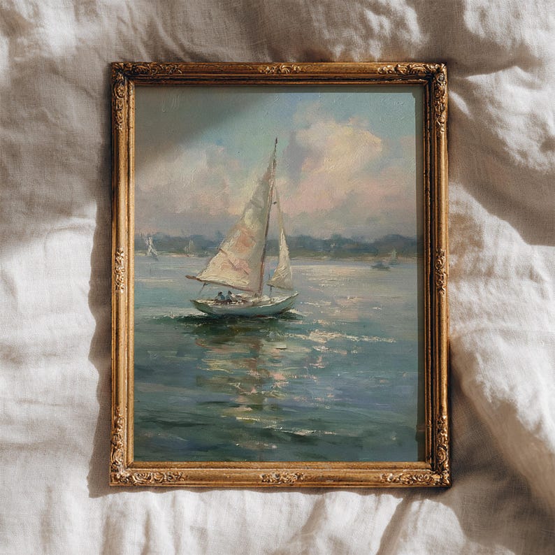 May include: A framed oil painting depicting a sailboat on calm water under a soft, cloudy sky. The artwork is enclosed in an ornate, metallic gold-toned rectangular frame with intricate embossed detailing along the edges and corners.