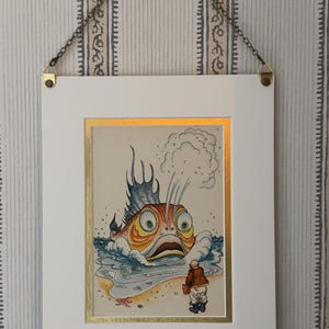 May include: Framed art print featuring a whimsical illustration of a large, surprised fish emerging from the water, facing a small figure on the shore. The artwork is framed in white with a gold border and hangs from a chain.