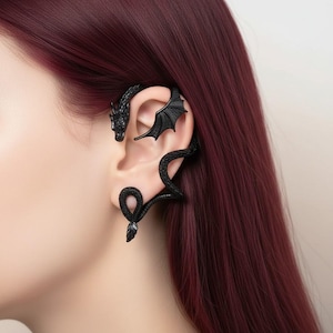 May include: Black dragon ear cuff. The cuff wraps around the ear, featuring a dragon head, wing, and a serpentine body. The dragon is a dark, matte black colour. The ear cuff is a unique piece of jewellery.