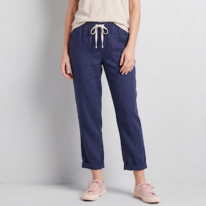 May include: Navy blue linen trousers with a drawstring waist and turned-up cuffs. The trousers are worn with a light-coloured top and pink trainers. The fabric appears to be lightweight.