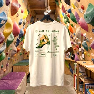Könnte beinhalten: Ein weißes T-Shirt mit einer grünen Grafik auf der Rückseite. Das Design zeigt eine Hand, die einen Griff hält, den Text FULL CRIMP, V 2.3 und Low GRAVITY sowie abstrakte geometrische Formen und Linien in einem strukturierten Layout.