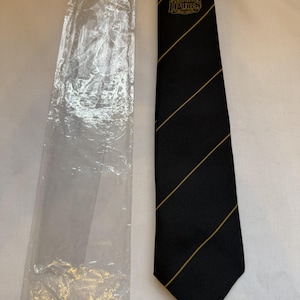 May include: Black tie with gold diagonal stripes and a logo that reads "The Brewers' Pubs". The tie is next to a clear plastic sleeve. The tie is likely made of a woven fabric.