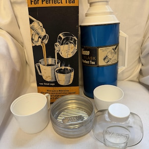 Op de afbeelding: Een witte keramische mok met een zwart handvat en de tekst "But First, Coffee" in een zwarte, handgeschreven lettertype. De mok staat op een wit oppervlak.