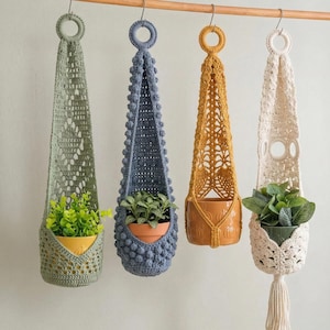May include: Four handmade crochet plant hangers in green, blue, gold, and cream, each holding a small potted plant. The hangers are suspended from a wooden rod, showcasing intricate openwork designs and varying textures, ideal for indoor decor.