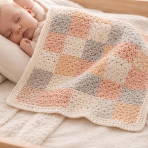 Può includere: Una coperta per neonati all'uncinetto fatta a mano con un design patchwork. La coperta presenta quadrati color crema, rosa, pesca e grigio. La coperta è morbida e accogliente, perfetta per un neonato. Ha un bordo color crema.