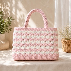 May include: A handmade crochet tote bag in a pink and white chevron pattern. The bag has a rectangular shape with a sturdy handle and a matching pink trim. The bag is sitting on a neutral surface.