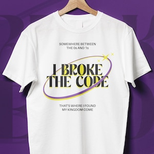Könnte beinhalten: Weißes T-Shirt mit dem Text "SOMEWHERE BETWEEN THE 0s AND 1s" über "I BROKE THE CODE" in einem lila und gelben Design. Darunter steht "THAT'S WHERE I FOUND MY KINGDOM COME".