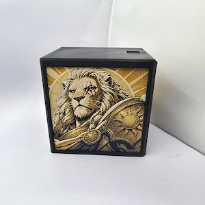 May include: A black square box featuring a detailed illustration of a lion warrior on the front panel. The lion has a thick mane and wears armor with a sun emblem. The background behind the lion is a golden sunburst pattern with rays.